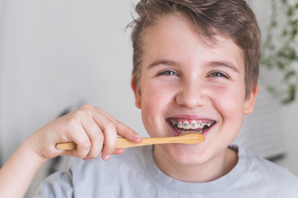 Little boy with brown hair brushing his teeth with braces and smiling