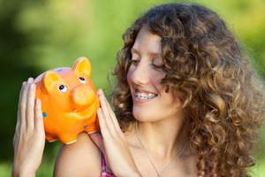 Woman with braces looking at a piggy bank